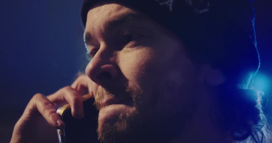 A cinematic close-up of a man wearing a beanie talking on his smartphone at night in slow motion