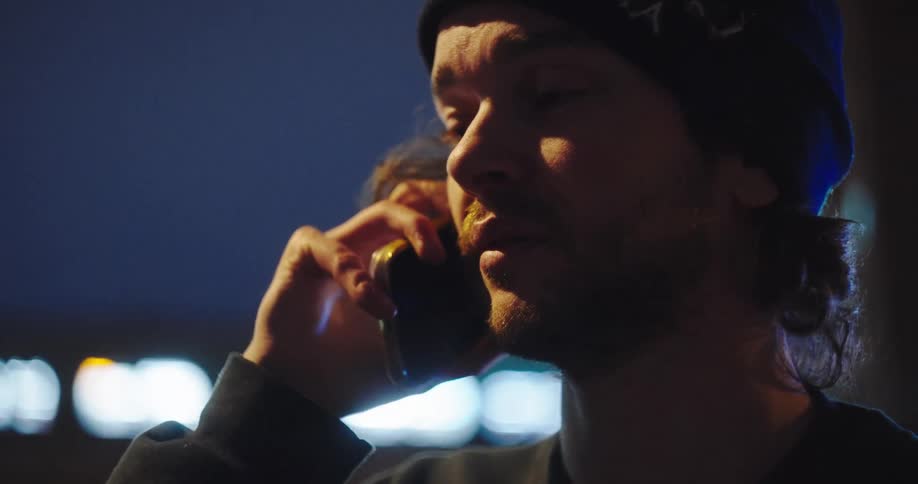 Close-up of a man in a beanie having a serious conversation on his phone at night in the city