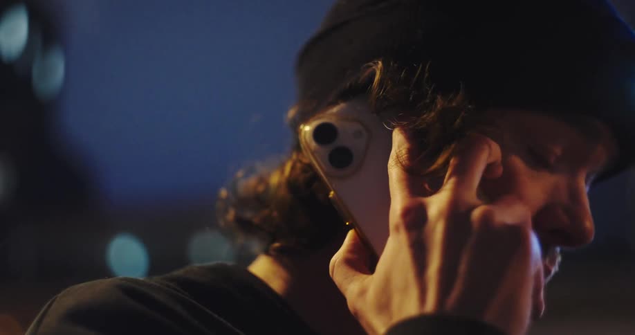 Close-up of a concerned man talking on his smartphone against the backdrop of city lights at night