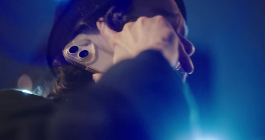 A distraught man in a beanie is overcome with emotion and cries while on a difficult phone call at night
