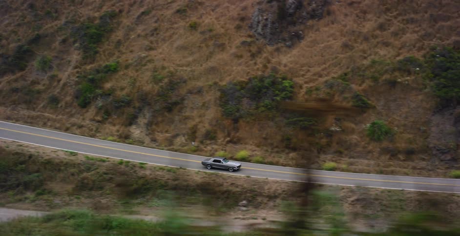 A classic grey muscle car takes a scenic drive along a winding highway through the mountains