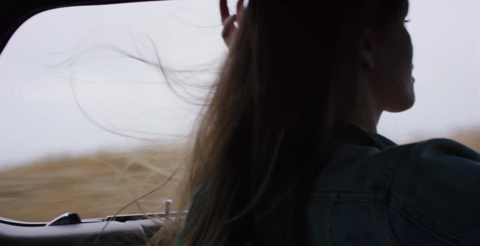 Slow motion shot of a woman's hair blowing in the wind as she drives a vintage car down a scenic coastal highway