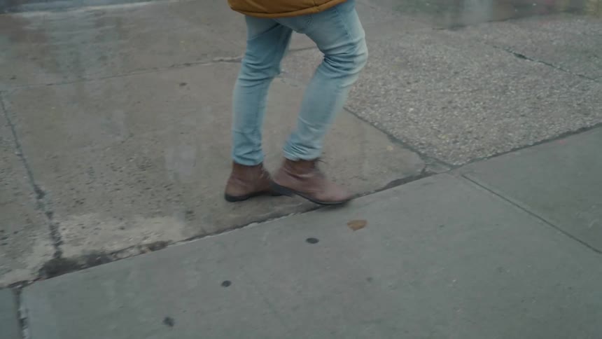 A man walks on a city sidewalk while it rains
