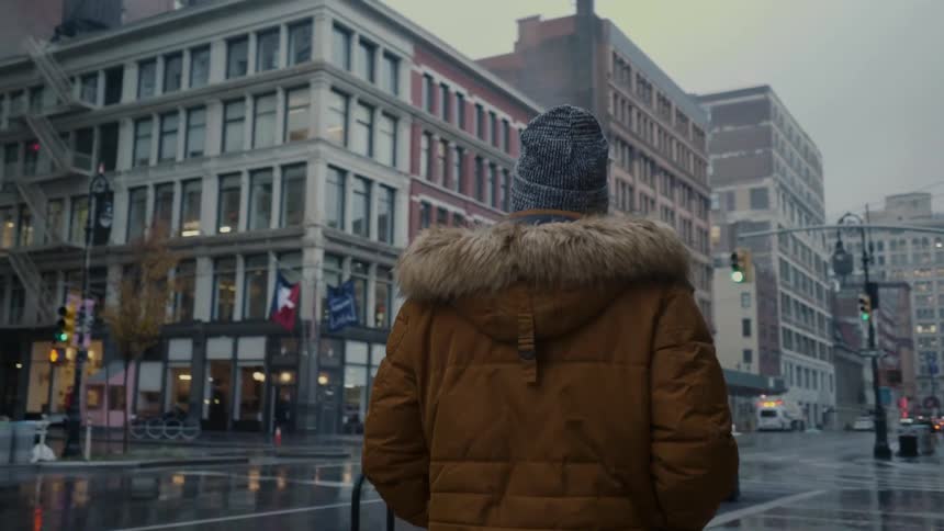 A boy in winter hat and coat walks a city sidewalk in the rain