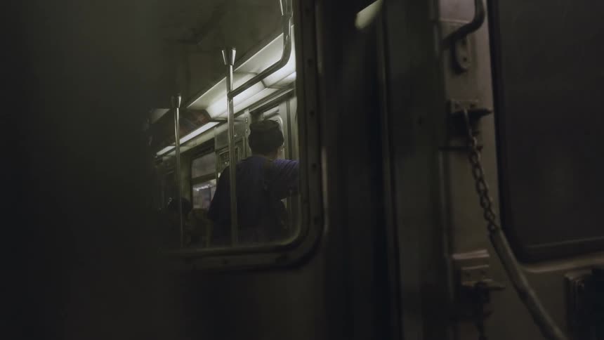 A man on a moving train stands looking out the door