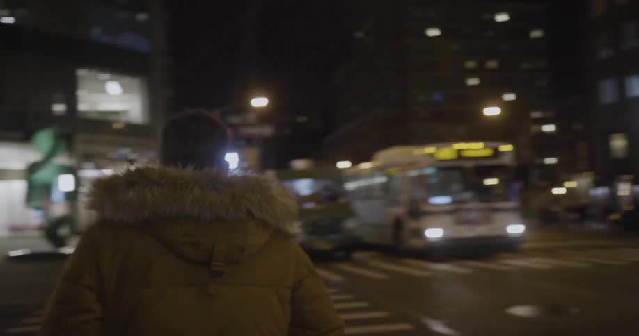 A man in a heavy coat crosses a city crosswalk at night
