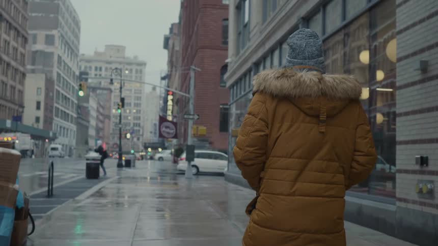 A man wears a heavy coat while walking on a city sidewalk on a rainy day