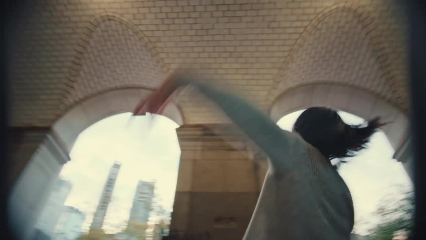 A graceful female dancer performs an expressive dance in slow motion under a beautiful arched, tiled ceiling in a city park