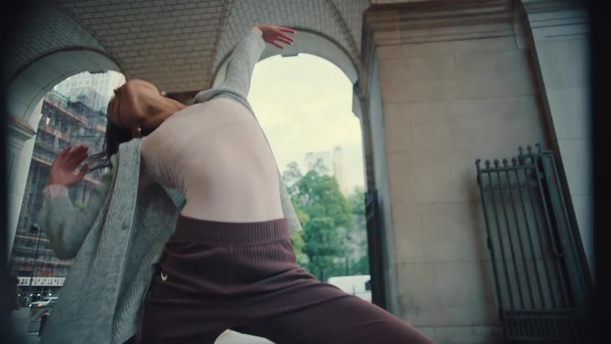 A graceful woman performs an expressive contemporary dance in slow motion under a classic city archway