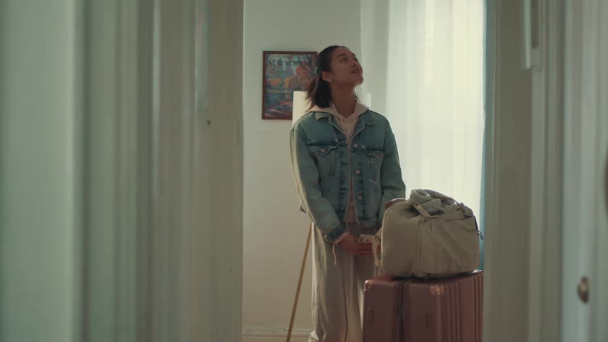 A happy young woman arrives with her luggage, looks around in awe, and then jumps for joy in her new apartment