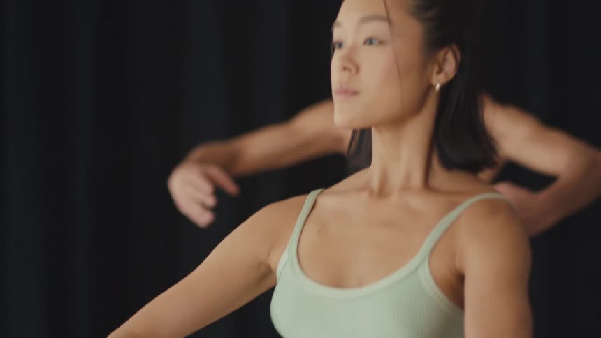 A graceful female ballet dancer practices a contemporary routine with her troupe in a studio in slow motion
