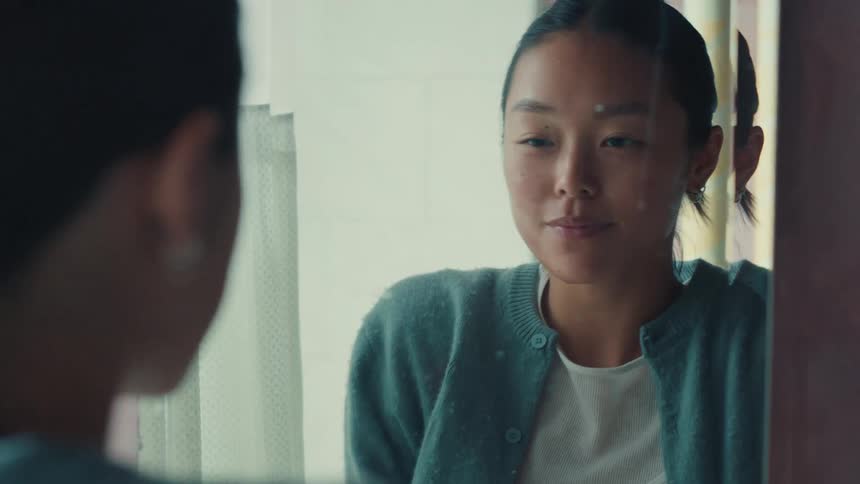 A young woman with acne cream on her face looks at her reflection in the mirror and smiles in a moment of self-acceptance