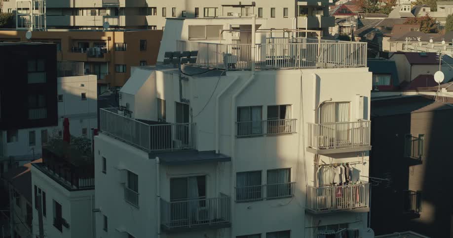 Laundry hangs to dry on the balcony of a white apartment building in a dense urban neighborhood during golden hour