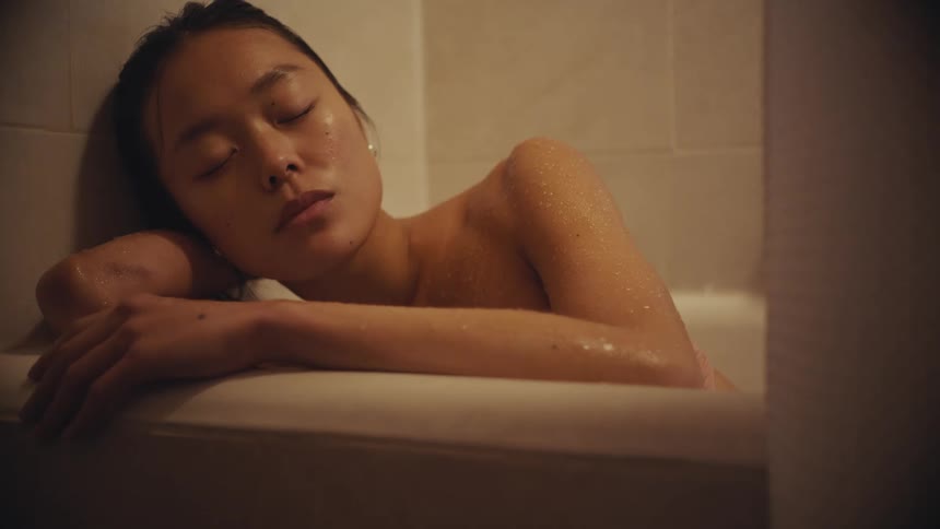 A cinemagraph shows a still shot of a young woman sleeping in a bathtub with water droplets on her skin