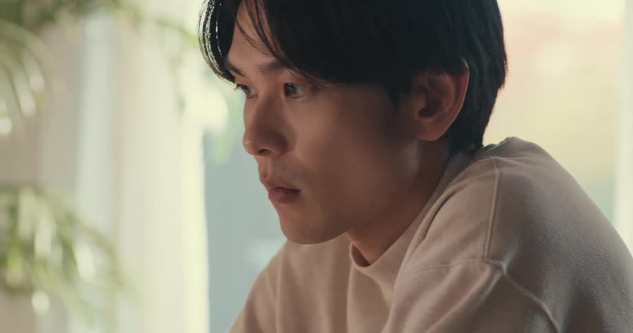 Close up of a pensive young Asian man with a serious expression as he concentrates on his work indoors