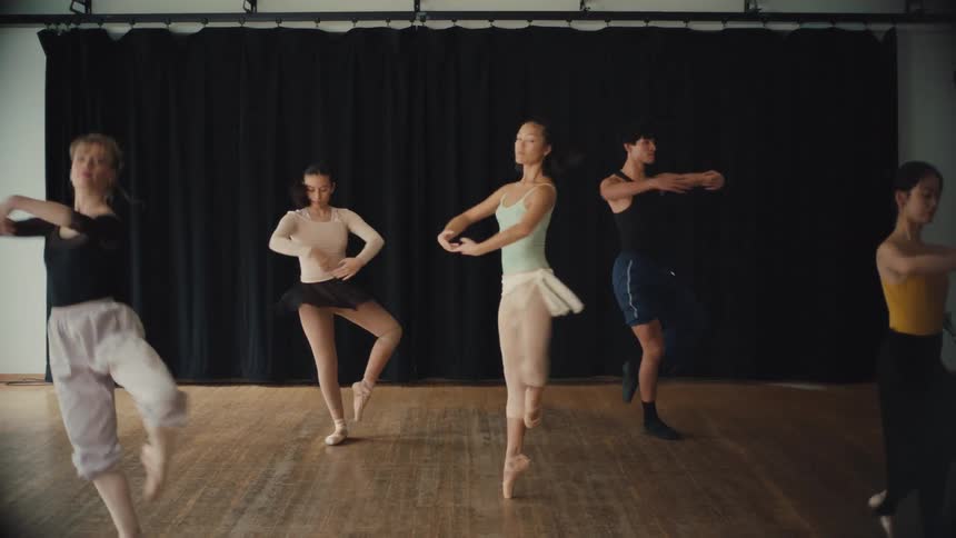 A diverse group of ballet dancers gracefully rehearse a synchronized routine in a naturally lit dance studio