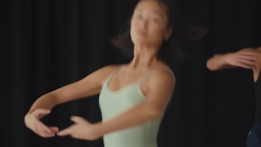 Slow motion close-up of a focused Asian ballerina practicing elegant and fluid contemporary dance movements in a studio