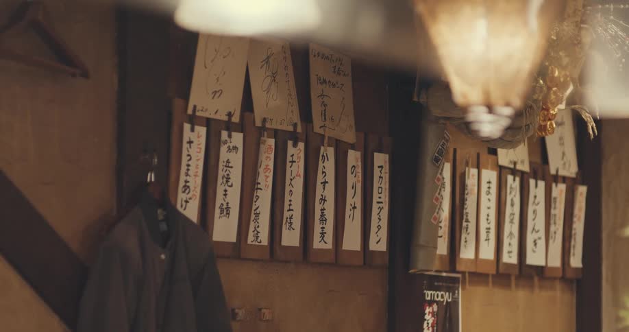 A handwritten menu and celebrity autographs adorn the wall of an authentic, dimly lit Japanese izakaya