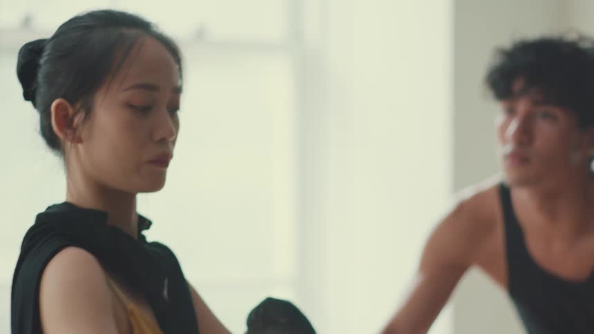 An elegant female dancer with her hair in a bun gracefully stretches in slow motion during a rehearsal in a bright studio