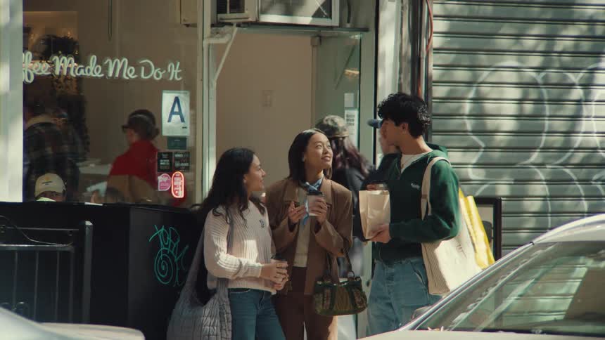 A group of happy young friends talk and laugh together while drinking coffee on a sunny city street