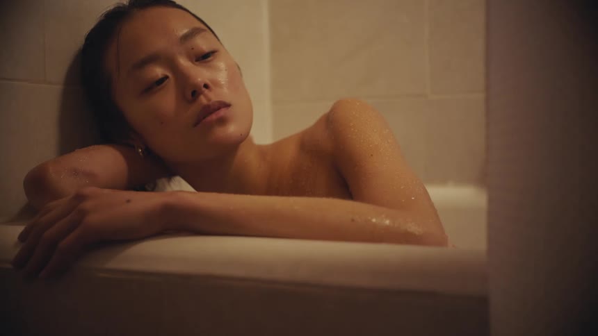 A pensive young woman finds a moment of quiet contemplation while resting in a dimly lit bathtub