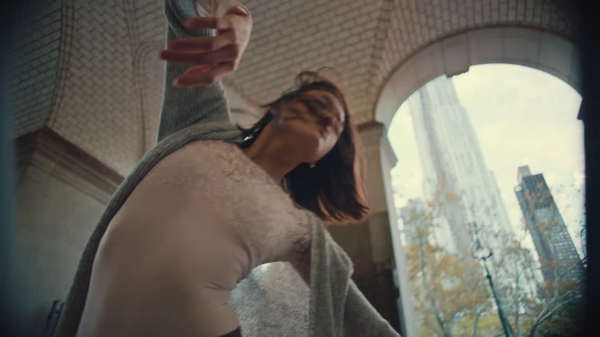 A graceful female dancer performs an expressive contemporary dance under a grand city archway in slow motion
