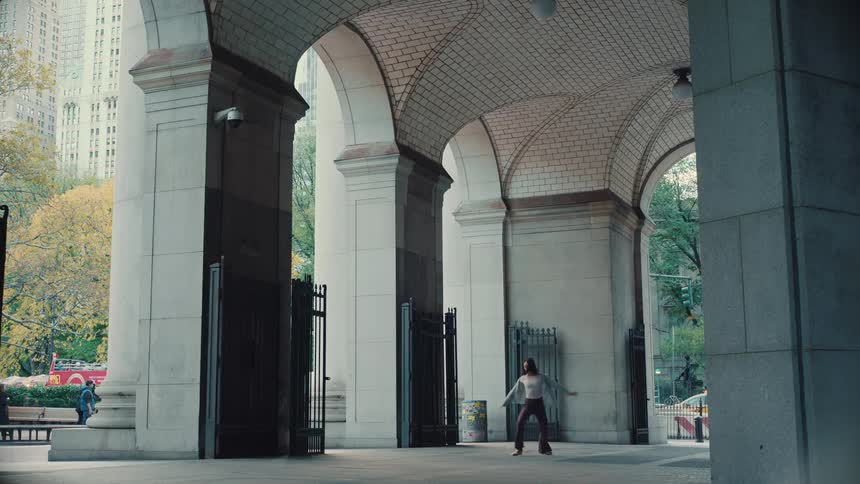A graceful woman performs an expressive contemporary ballet dance under a grand arched stone entryway in a city park