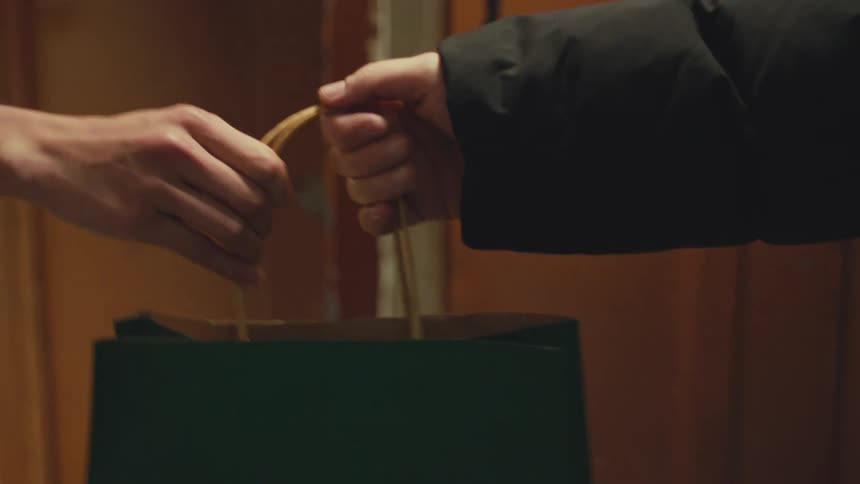 Slow-motion close-up of one person handing a green paper gift bag to another person indoors