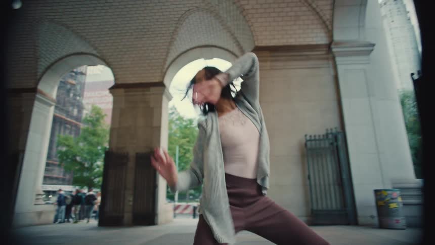 A graceful young woman performs an expressive modern ballet routine in slow motion under a grand city archway