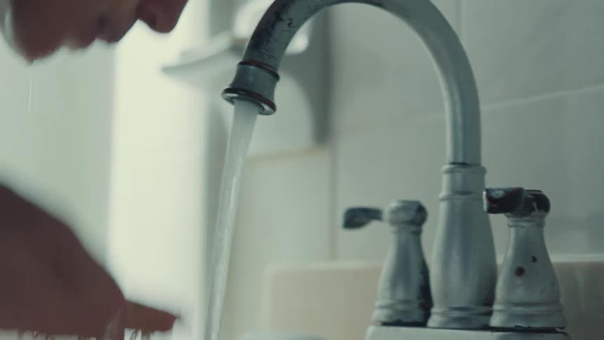 Close-up of a person turning on an old bathroom faucet, splashing water on their face, and turning it off in slow motion