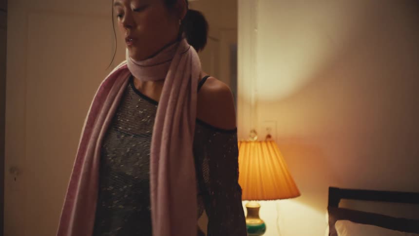 A tired young woman comes home, enters her dimly lit room, and sits down to look at her phone in slow motion