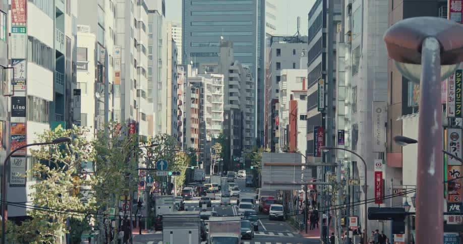 A long shot captures the daytime hustle and bustle of a busy street in a modern Japanese city