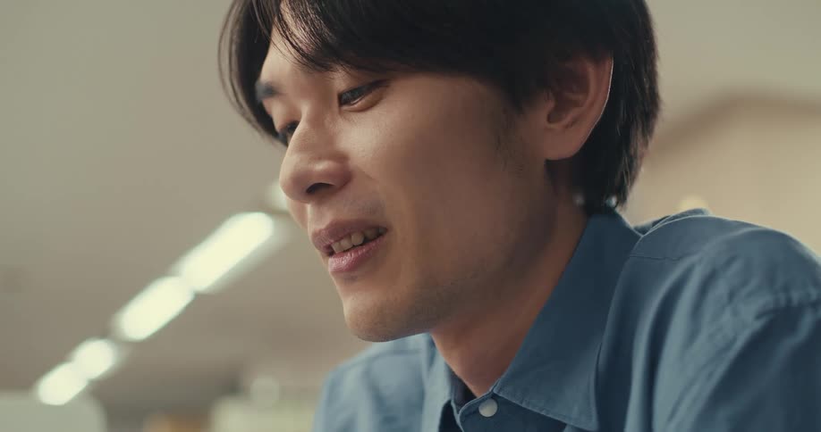 A close-up of a young Asian man smiling contentedly while concentrating on a task
