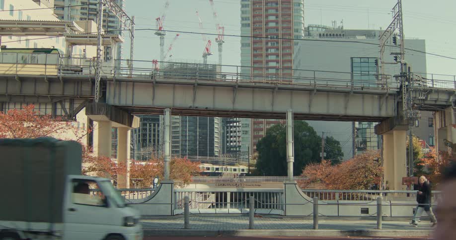 The daily life of a modern Japanese city unfolds with trains, traffic, and pedestrians moving under a railway overpass