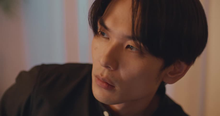 An intimate close-up shot of a thoughtful young Asian man looking off-camera with a serious expression