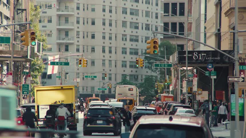 A slow zoom out reveals a busy intersection on Broadway in New York City, teeming with traffic and pedestrians