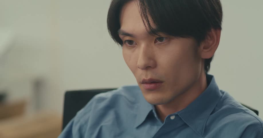 Close-up of a serious young Asian man with a focused expression concentrating on his work in an office