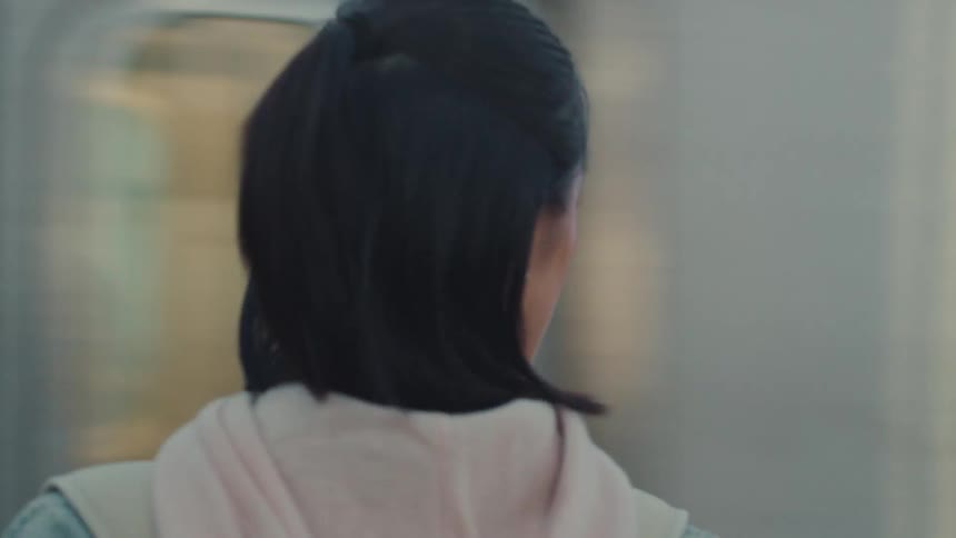 Close-up of an introspective young woman on a train platform as a subway car speeds past
