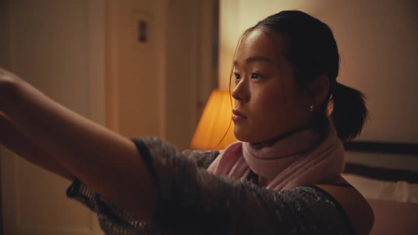 A stylish young Asian woman takes a selfie with her smartphone in her warmly lit bedroom, captured in slow motion