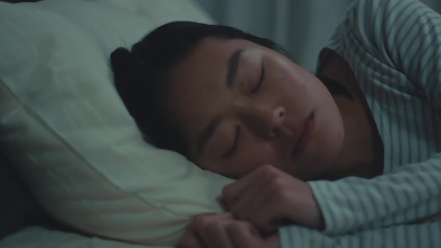 A beautiful young Asian woman in pajamas sleeps peacefully in her cozy bed at night, looking serene and comfortable
