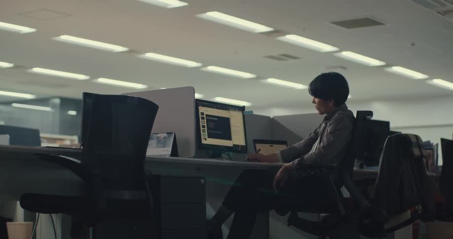 A young man in a modern office appears tired and stressed while working at his computer