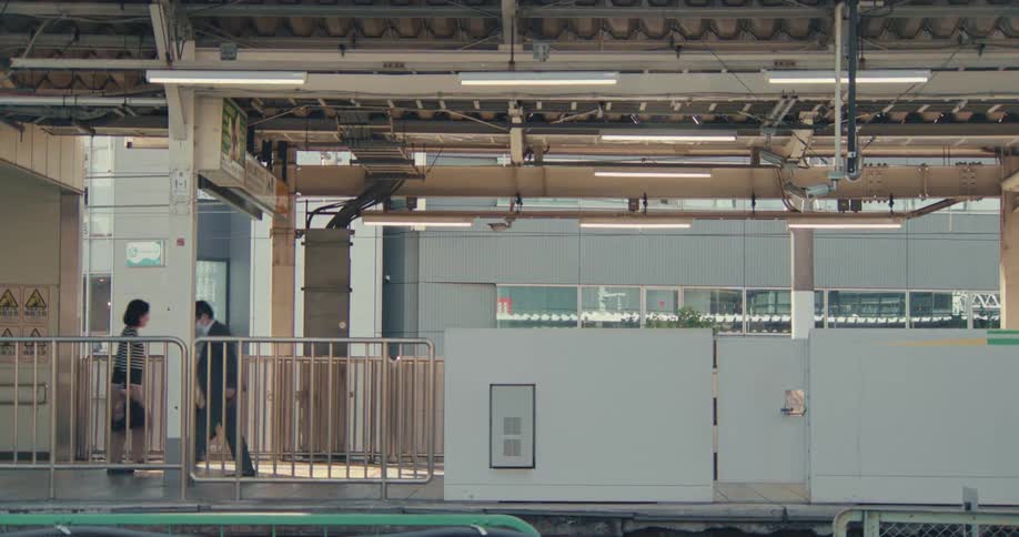 A Japanese bullet train creates a motion blur as it speeds through a station, with commuters walking on the platform