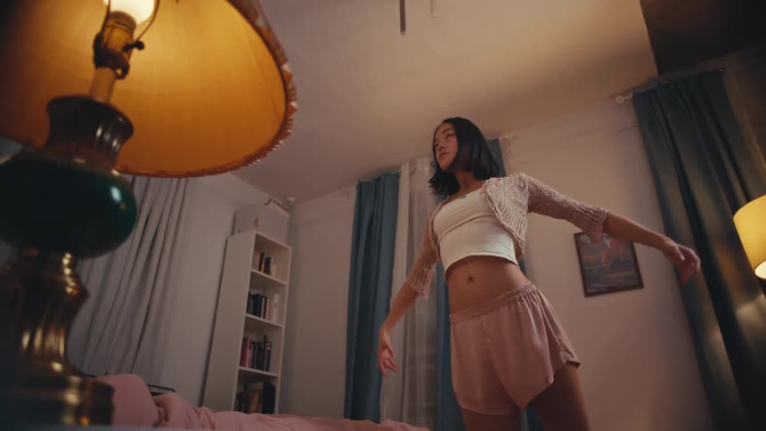 Low-angle shot of a young woman in pajamas gracefully dancing in her cozy, dimly lit bedroom at night
