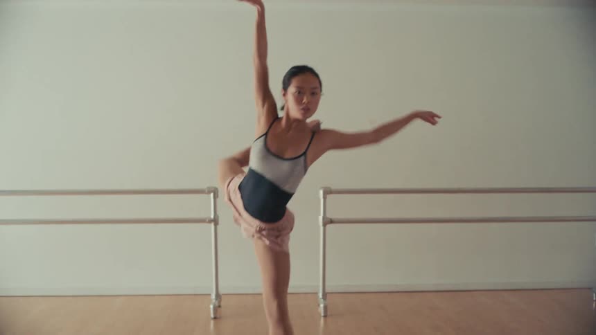 A graceful Asian ballerina performs a fluid and expressive contemporary ballet routine in a minimalist sunlit dance studio