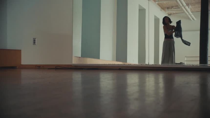 A woman gets dressed, cleans the floor, and leaves an empty dance studio after practice