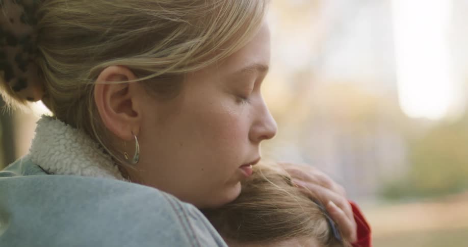 An intimate close-up shows a loving mother gently comforting her daughter with a warm embrace and a kiss