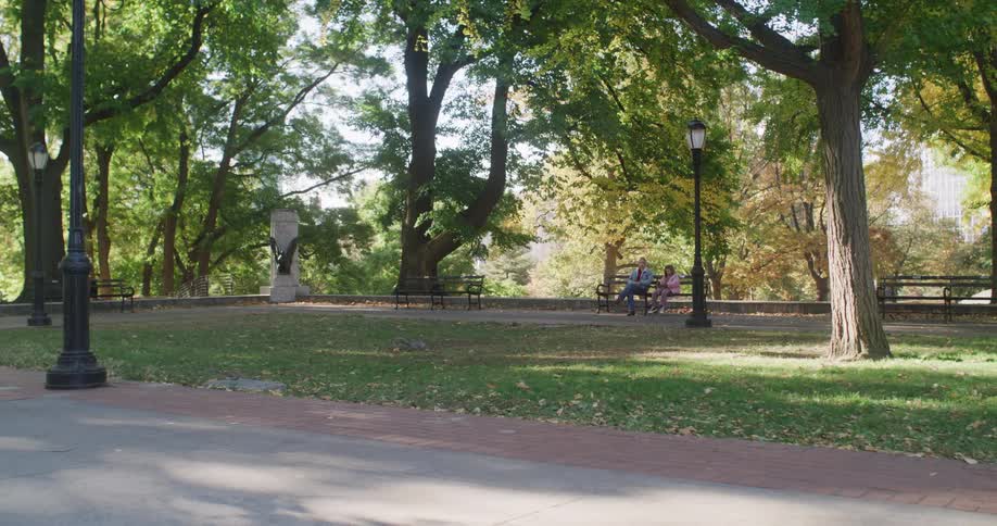A father and his young daughter sit and talk on a park bench under the trees on a beautiful sunny day