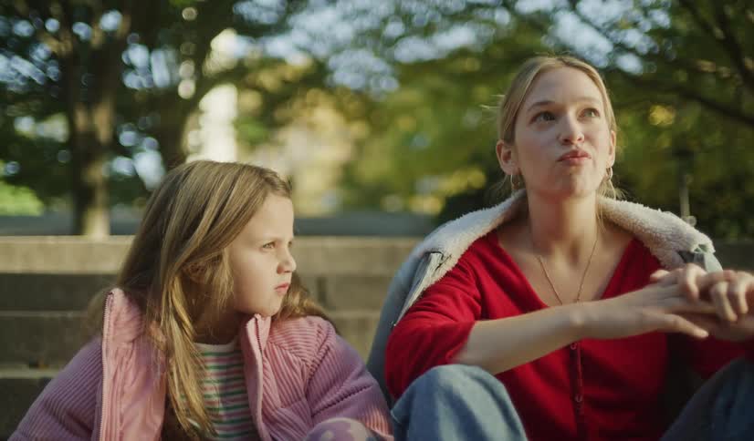 A mother and her young daughter sit on stone steps outdoors having a thoughtful conversation on a sunny day