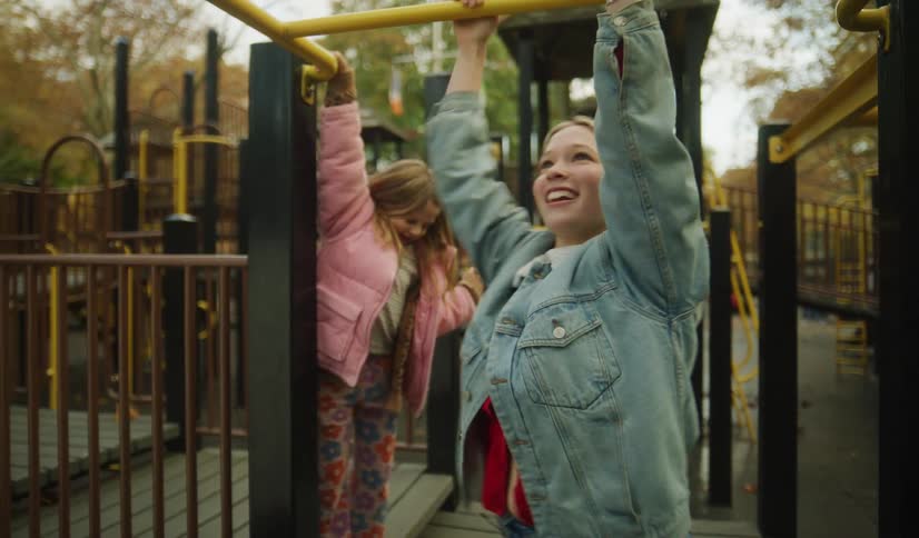 A happy young woman crosses the monkey bars in slow motion as a little girl watches and cheers her on at a playground