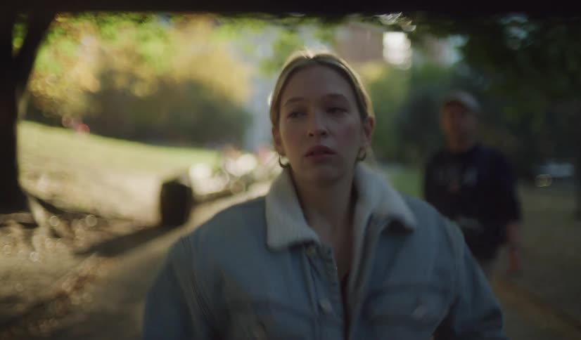 A sad young woman walks alone down a path in a sun-dappled park in slow motion